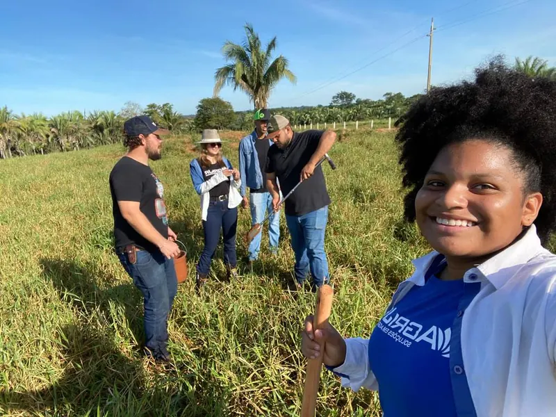 Equipe da AgriJr realizando coleta de amostras de solo em propriedade rural, com trator ao fundo